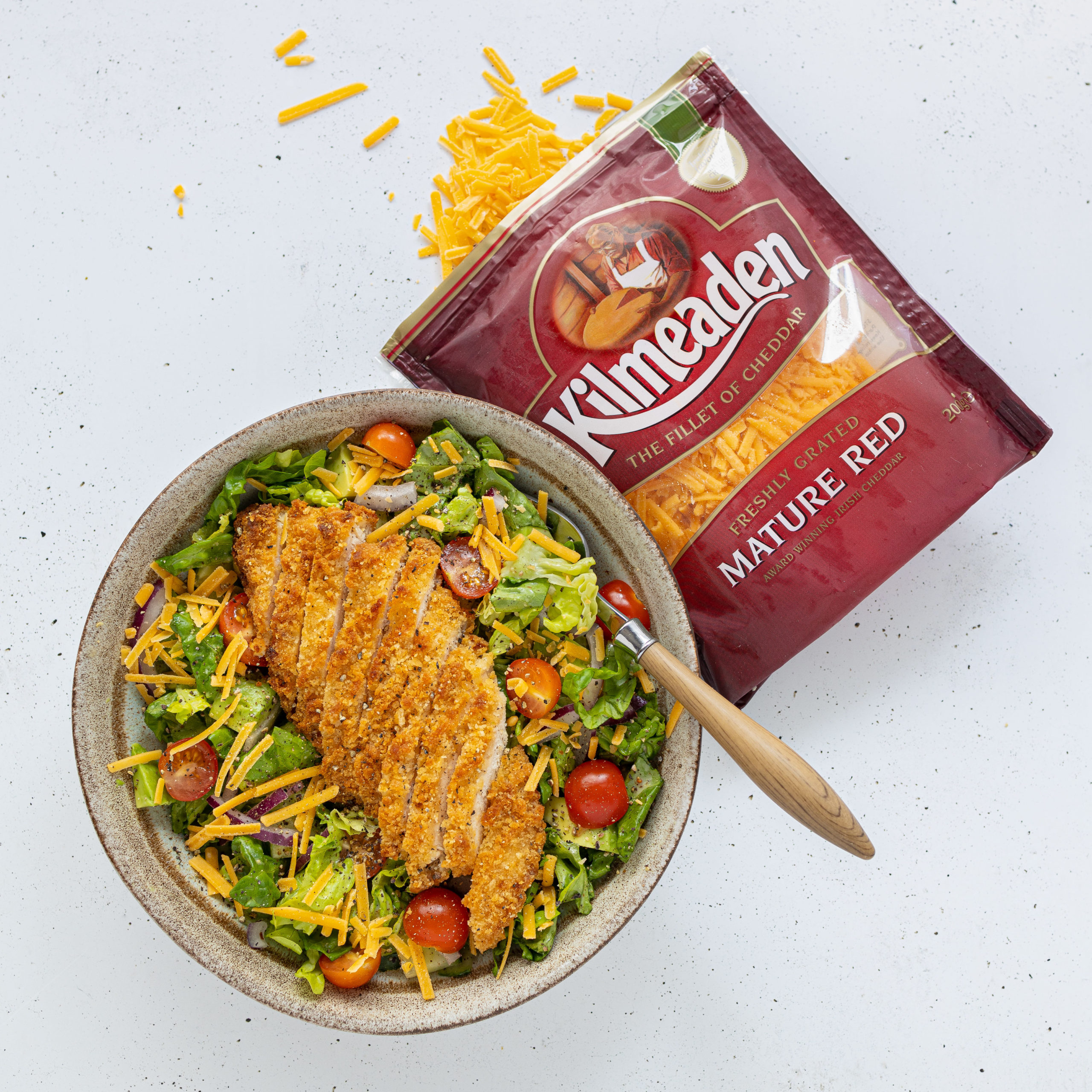 Breaded chicken salad with tomatoes and grated Kilmeadan Red Cheddar cheese beside 200 gram pouch of Kilmeaden Mature Red Cheddar Cheese.